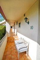 Un pasillo con piso de baldosas, paredes blancas y un cartel con el número 10. Hay sillas blancas a lo largo de la pared y una lámpara verde fijada a la pared.