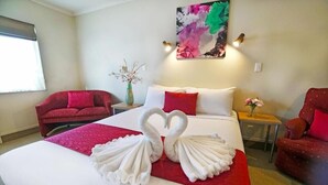 A hotel room with a bed, two red armchairs, a nightstand, and a painting on the wall. - Ashwood Manor Motor Lodge (Hamilton)