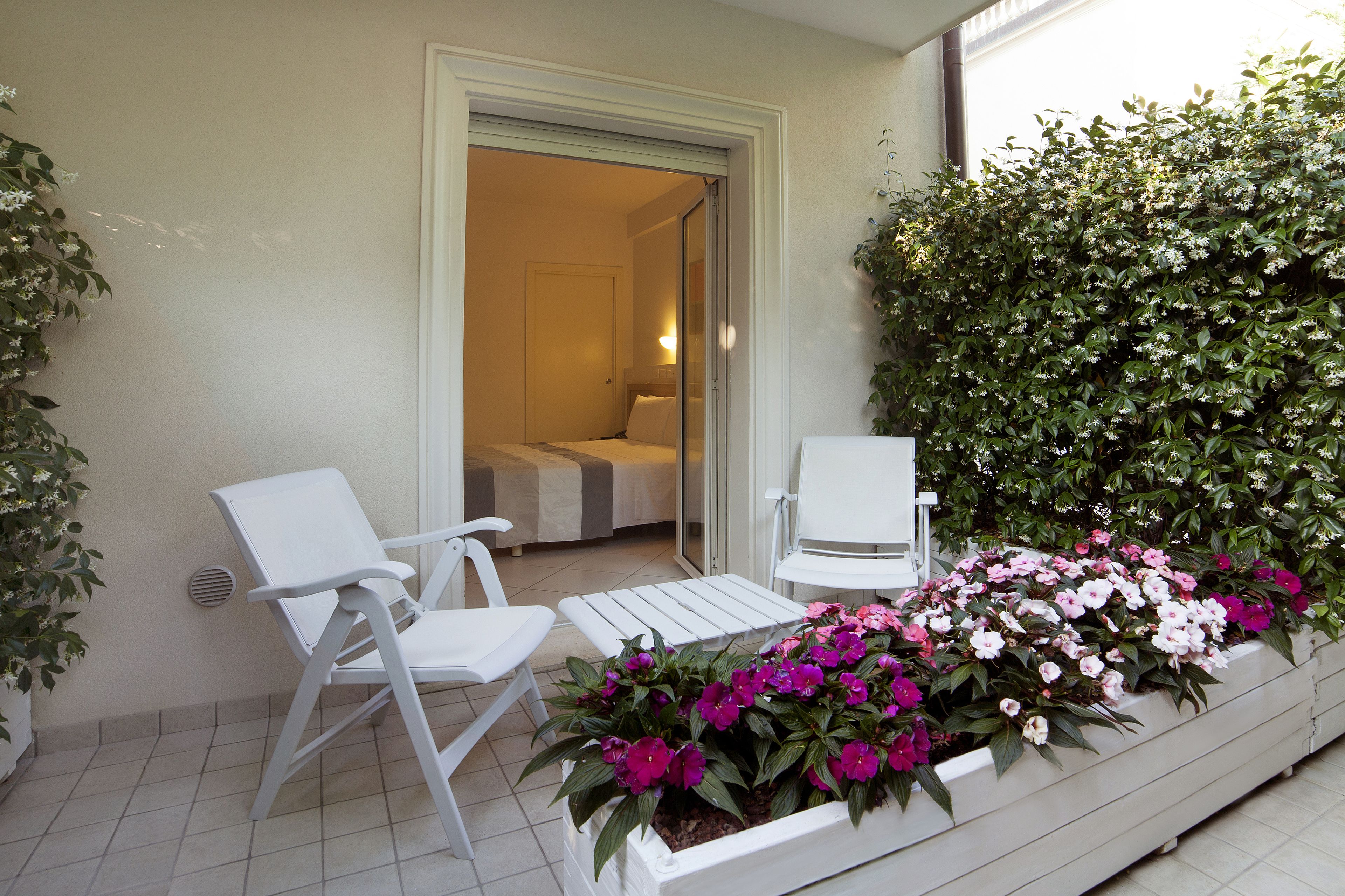 A balcony with two white chairs, a small table, and a planter with pink and white flowers.