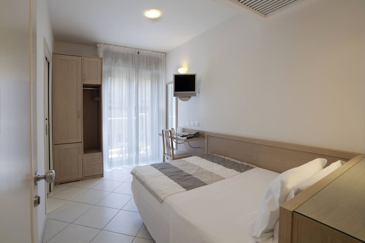 Une chambre d’hôtel équipée d’un lit, d’un bureau, d’une chaise, d’une armoire et d’un téléviseur fixé au mur.