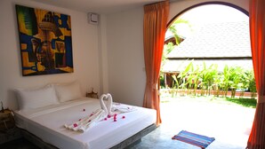 A bed with white linens, a painting on the wall, and a view of greenery through an open doorway. - Wazzah Resort (Koh Samui)