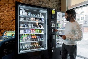 Een persoon bedient zich van een automaat gevuld met verschillende dranken en snacks.