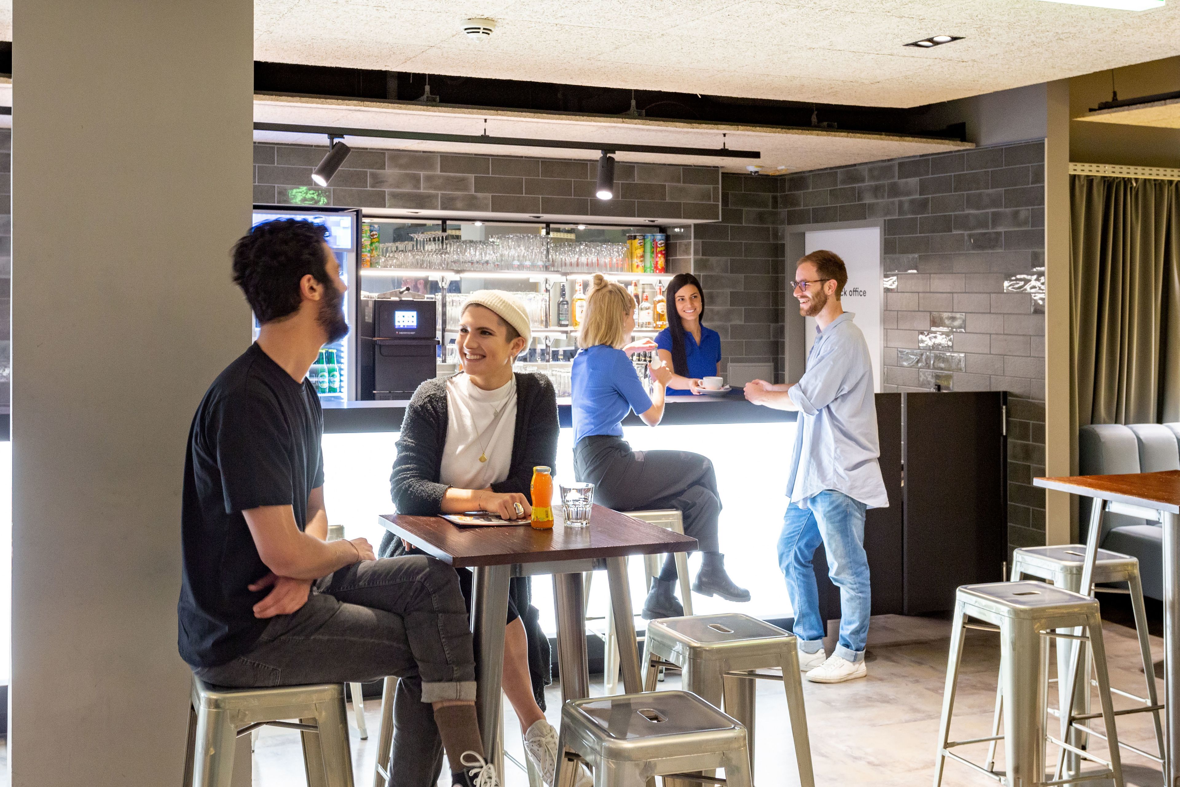 A group of people in a modern indoor setting with a bar area, seating, and a whiteboard.