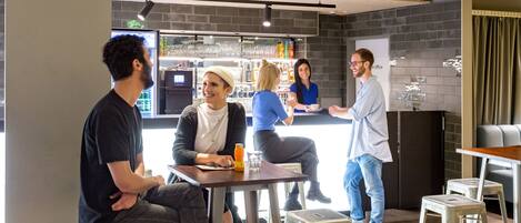 A group of people in a modern indoor setting with a bar area, seating, and a whiteboard.