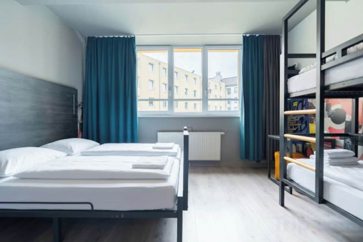 A room with two beds, a bunk bed, a window with curtains, and a radiator.