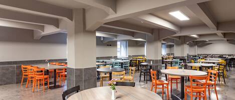 A spacious cafeteria with multiple tables and chairs, featuring a modern architectural design with exposed beams and a neutral color palette.