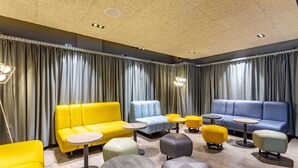 A modern lounge area with sofas and ottomans in yellow, blue, and gray, arranged around small round tables. - a&o Wien Hauptbahnhof (Vienna)