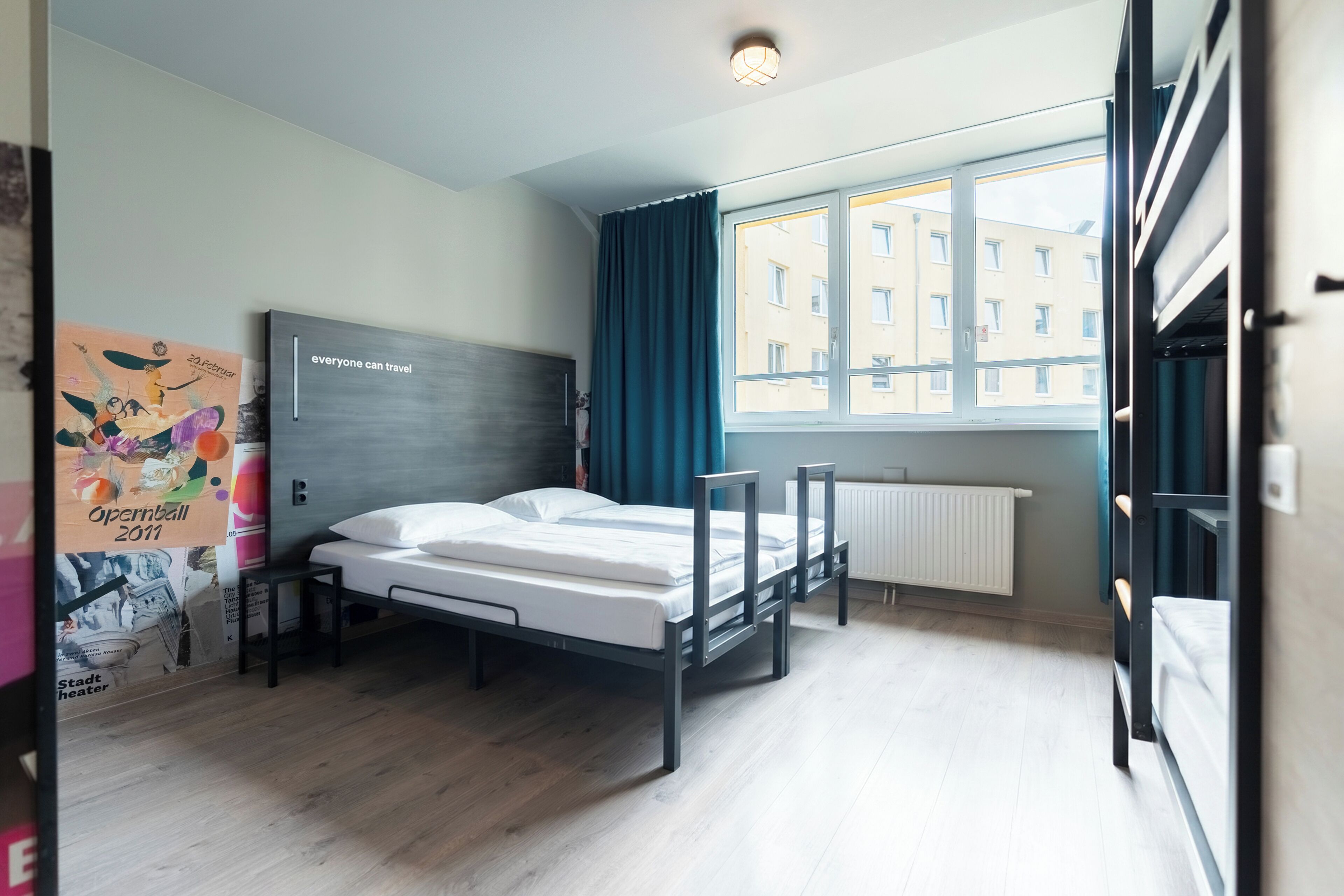 A modern hotel room with a bed, a window with curtains, a radiator, and a poster on the wall.