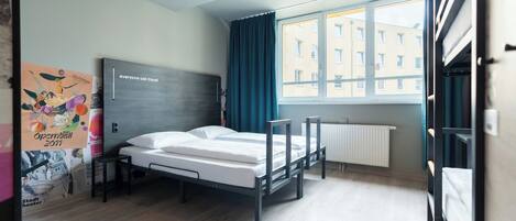 A modern hotel room with a bed, a window with curtains, a radiator, and a poster on the wall.