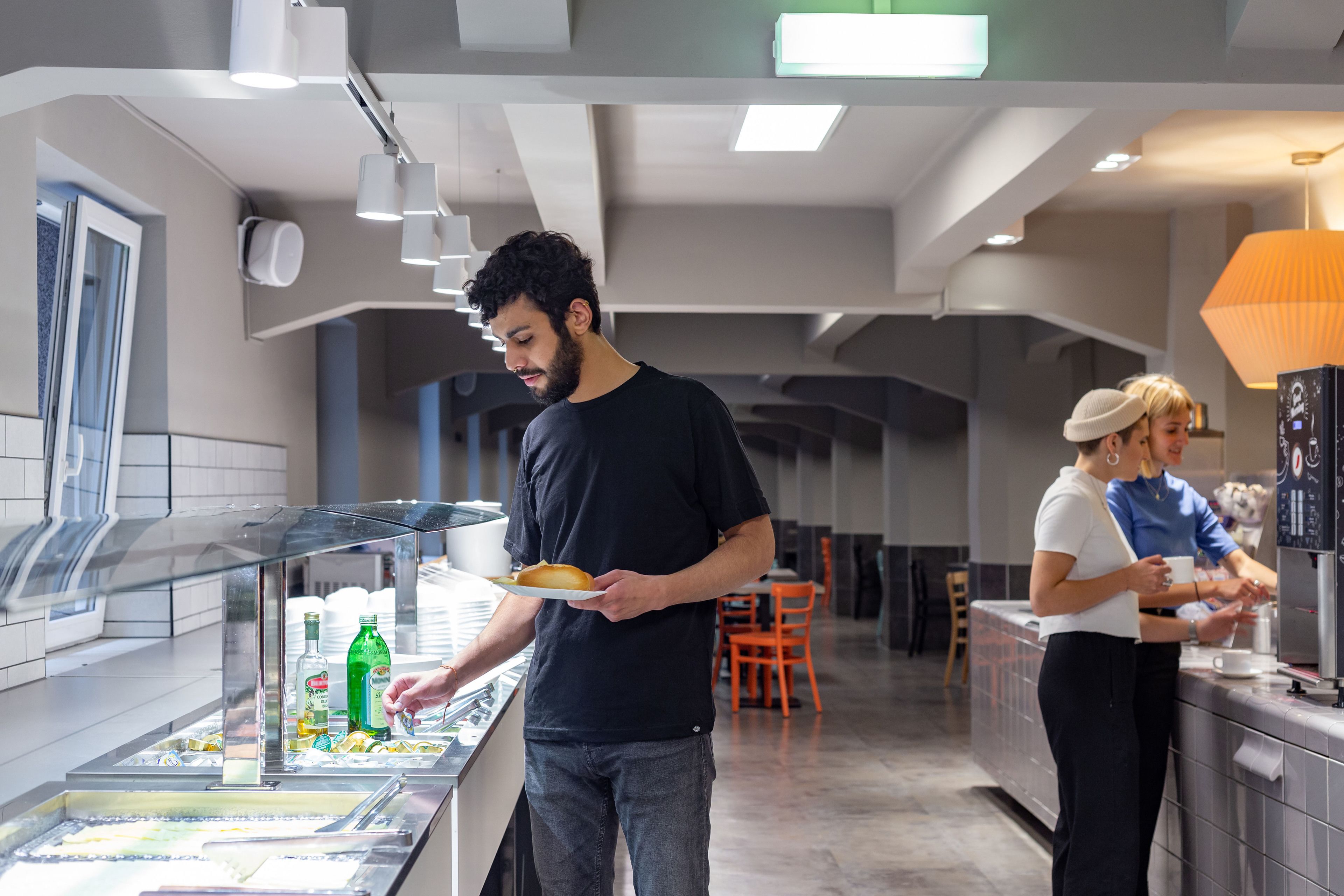 Un restaurante moderno con una barra de helados de autoservicio, una zona de estar con sillas color naranja y una persona atendiendo.