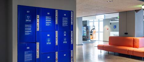 A hotel lobby with blue lockers numbered 317 to 318, an orange sofa, and an ATM.