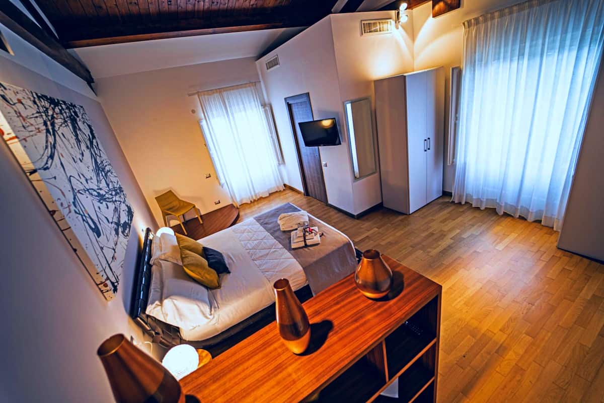 A hotel room with a bed, a wooden table with vases, a TV, and a large abstract painting on the wall.
