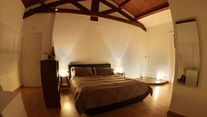 A bedroom with a wooden ceiling, a large bed, bedside lamps, and a mirror on the wall. - Hotel Cave del Sole (Matera)