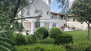 A covered outdoor seating area with white chairs and a table, surrounded by well-maintained greenery and a building with a tiled roof. - Hotel Cave del Sole (Matera)