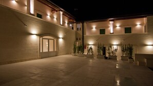 A spacious courtyard with a covered walkway, potted plants, and illuminated walls. - Hotel Cave del Sole (Matera)