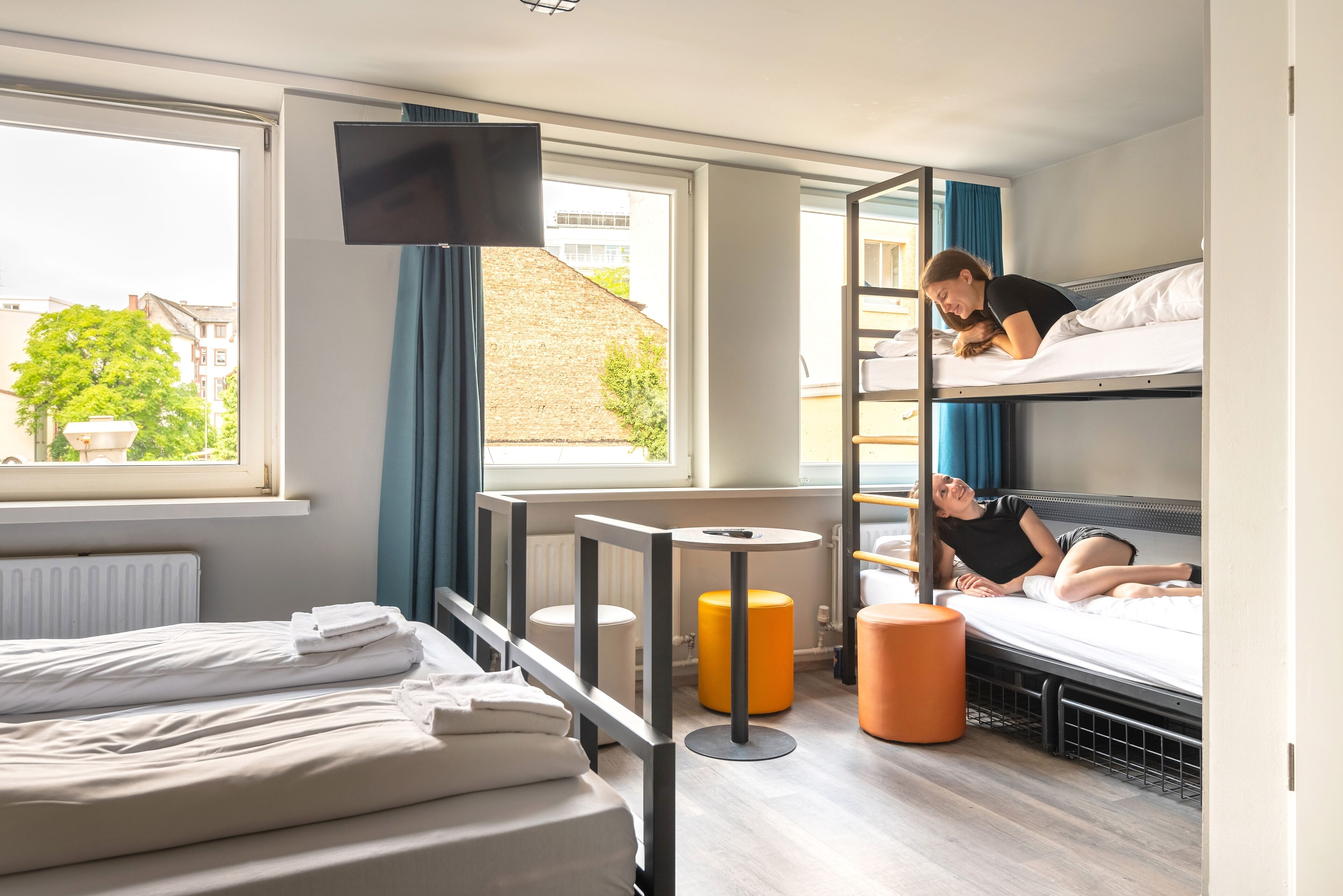 Habitación de hotel con literas, televisor, ventana con cortinas y radiador.