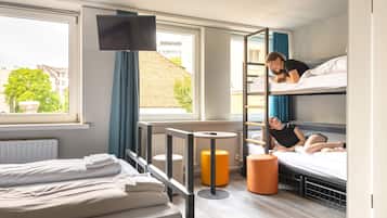 Habitación de hotel con literas, televisor, ventana con cortinas y radiador.