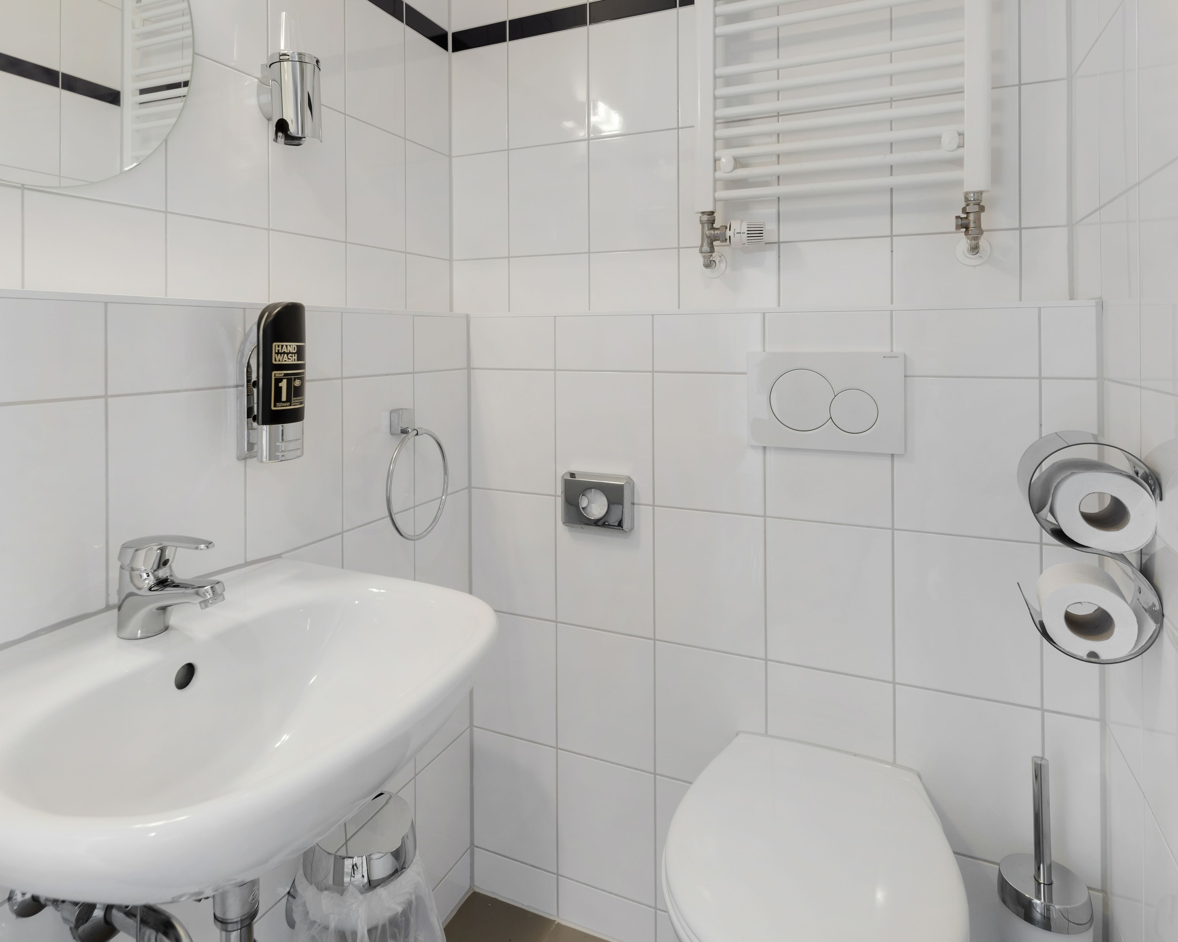 A modern bathroom with a white sink, toilet, and bidet, featuring chrome fixtures and white tiles.