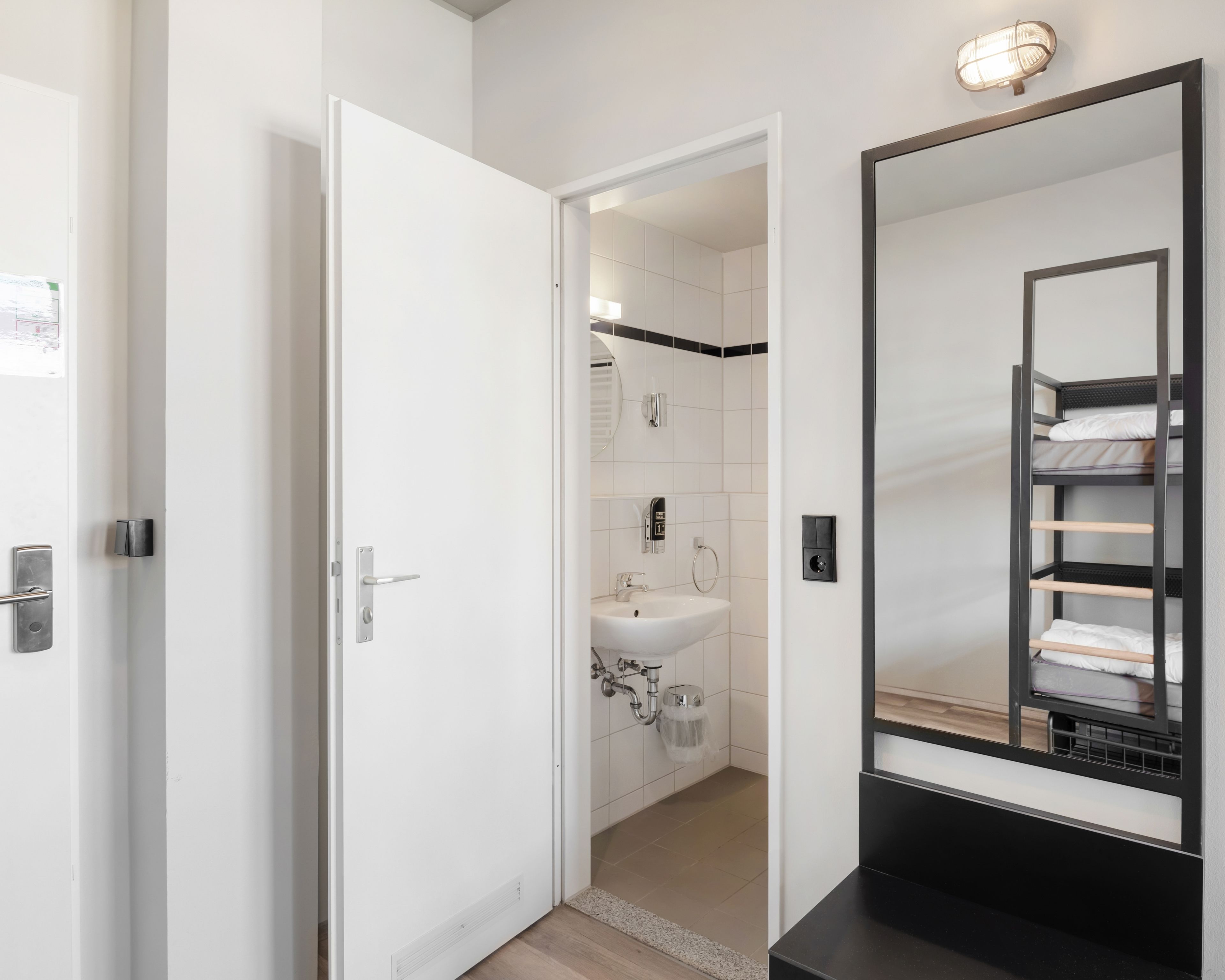 A hotel bathroom with a white sink, a mirror, and a black shelf with towels.