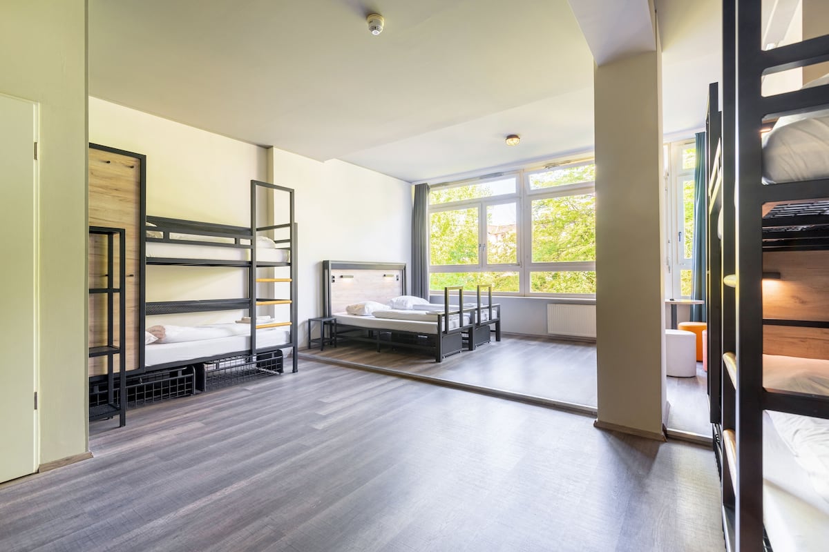 Une chambre de dortoir avec des lits superposés, une fenêtre donnant sur un espace verdoyant et une porte menant à une autre pièce.