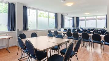 A conference room with multiple tables and chairs, large windows with curtains, and a ceiling with recessed lighting.