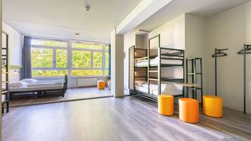 Una habitación de hotel moderna con un ventanal grande, literas y otomanas naranjas.