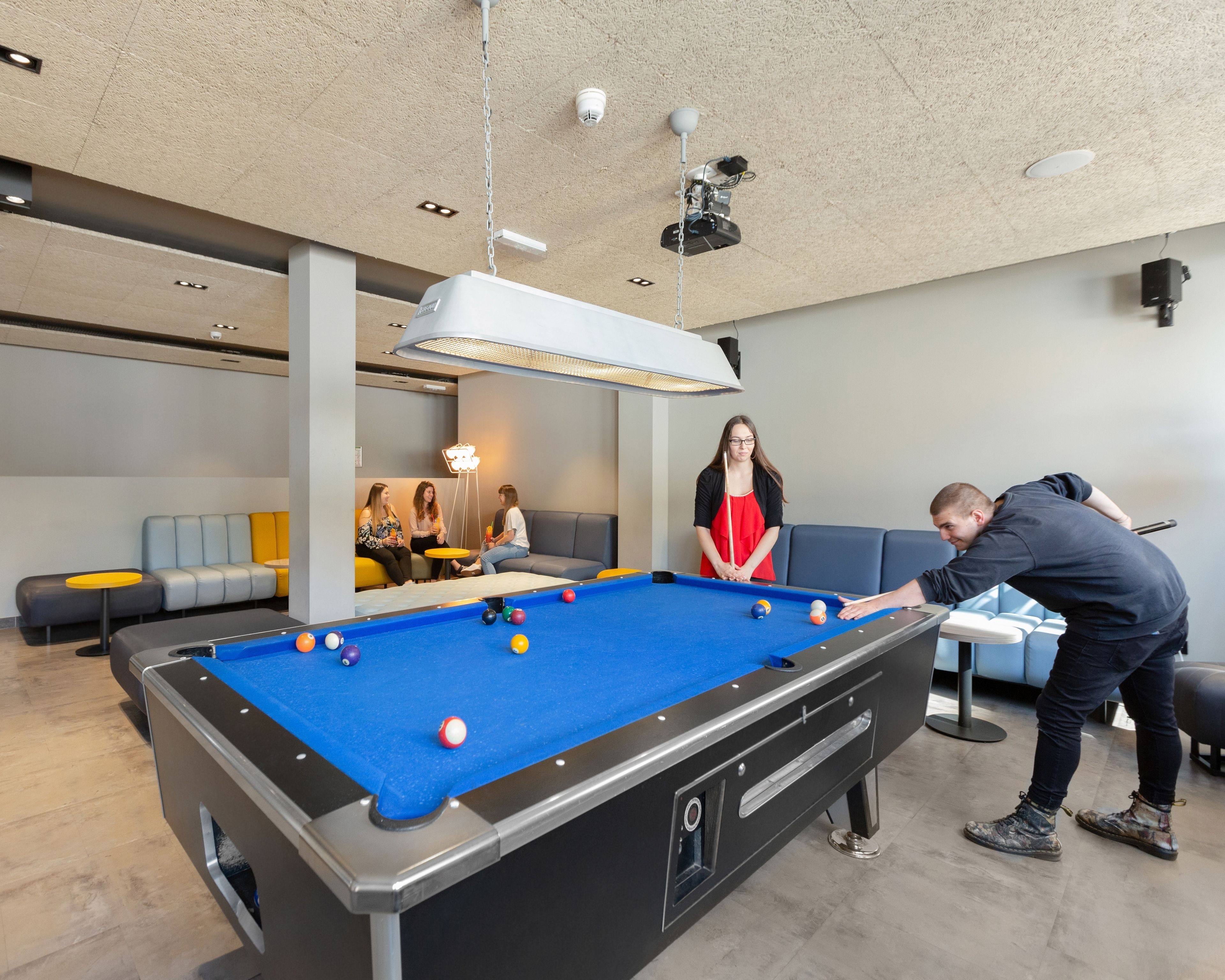 A pool table in a modern indoor setting with a sofa and a small table in the background.