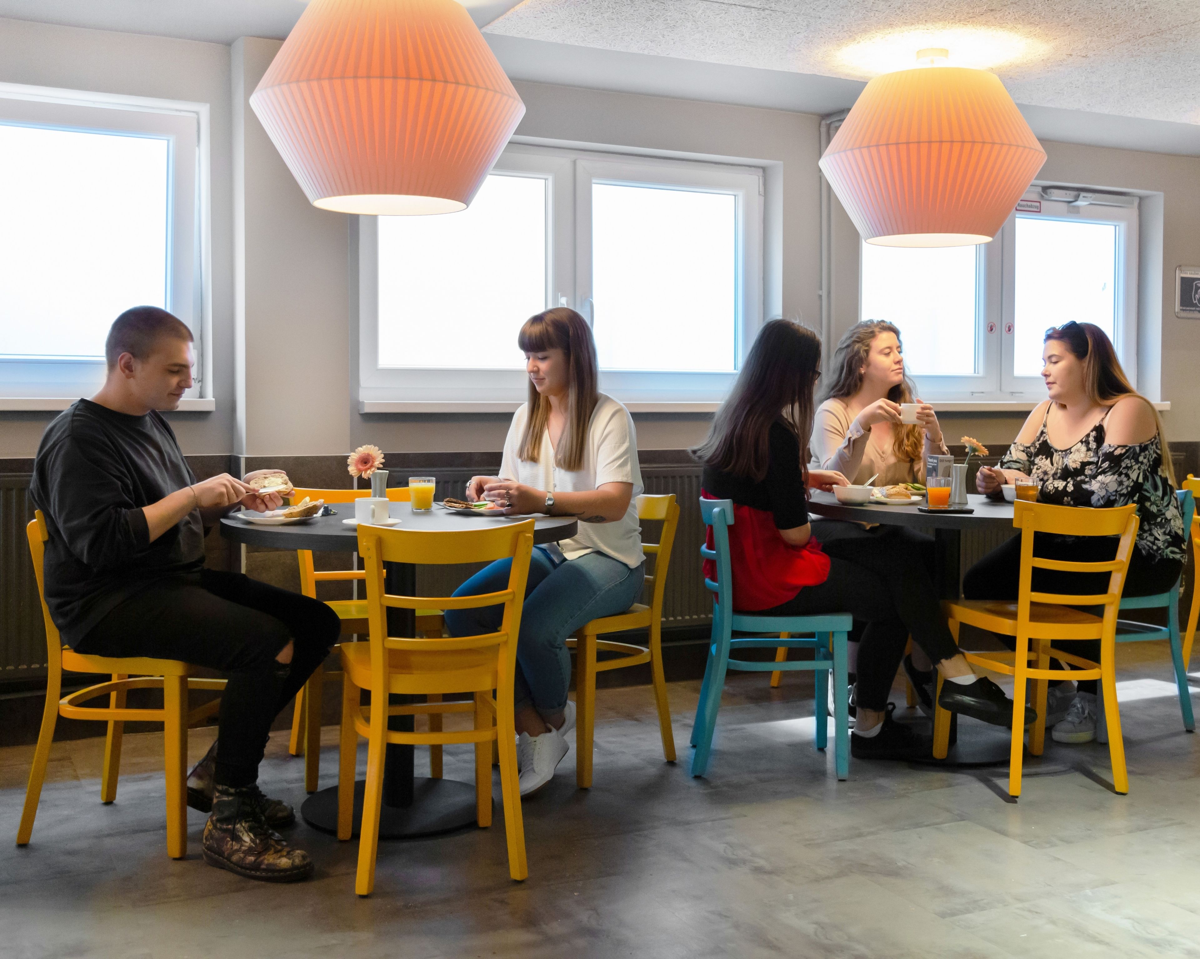 Een groep mensen dineert in een restaurant met gele stoelen en oranje hanglampen.