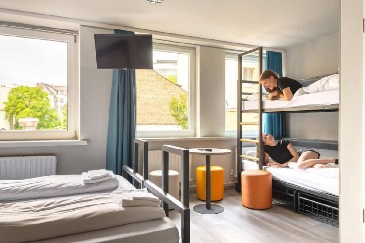Une chambre d’hôtel avec un lit, des lits superposés, une télévision et une fenêtre donnant sur un paysage agréable.