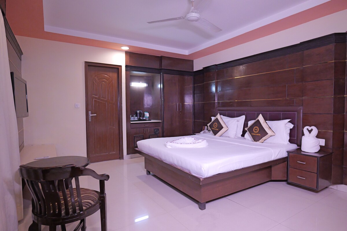 A hotel room with a large bed, a wooden headboard, a nightstand, a chair, and a ceiling fan.