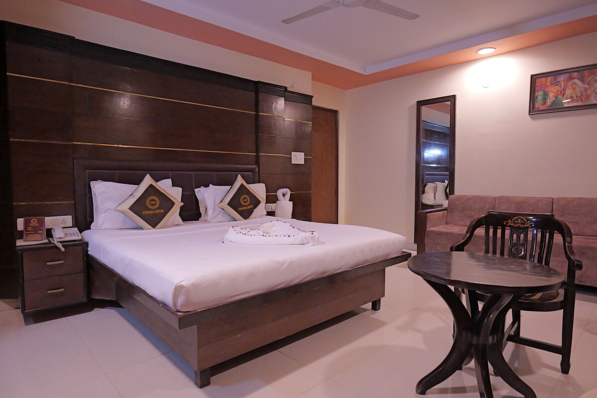 A hotel room with a large bed, bedside table, and a small round table with a chair.