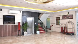 A hotel lobby with a modern chandelier, a flat-screen TV, a reception desk, a staircase, and a painting on the wall. - Foxoso Taj View Hotel (Agra)