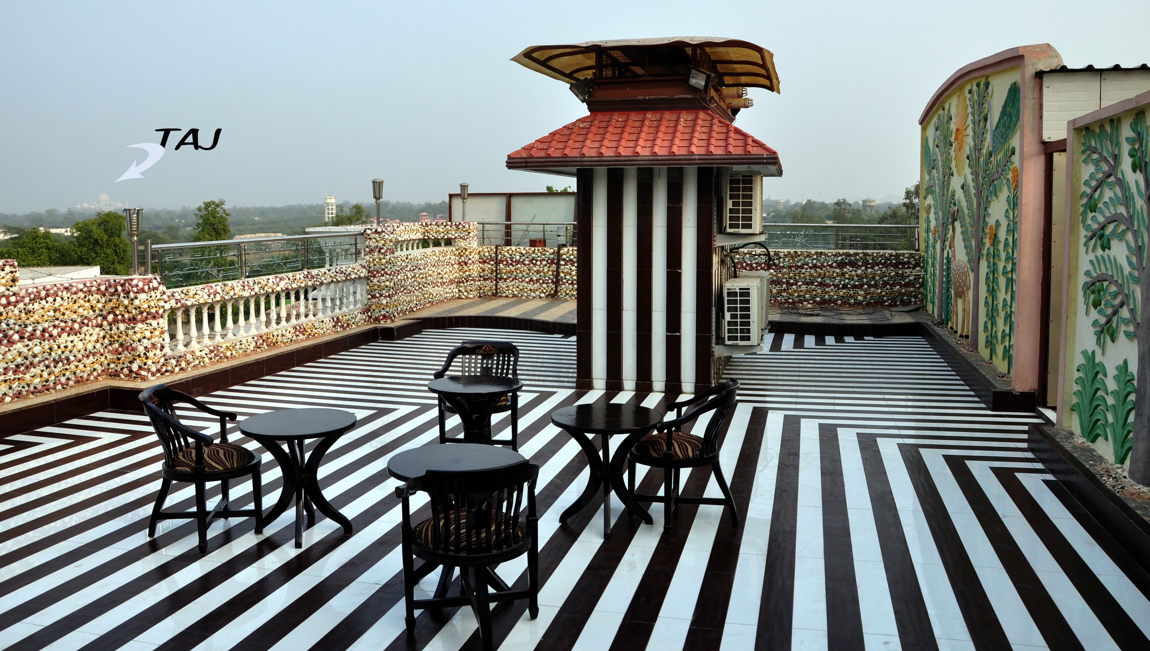 Una terrazza sul tetto con pavimento decorato, un piccolo tavolo con sedie e un muro ornamentale con un affresco.