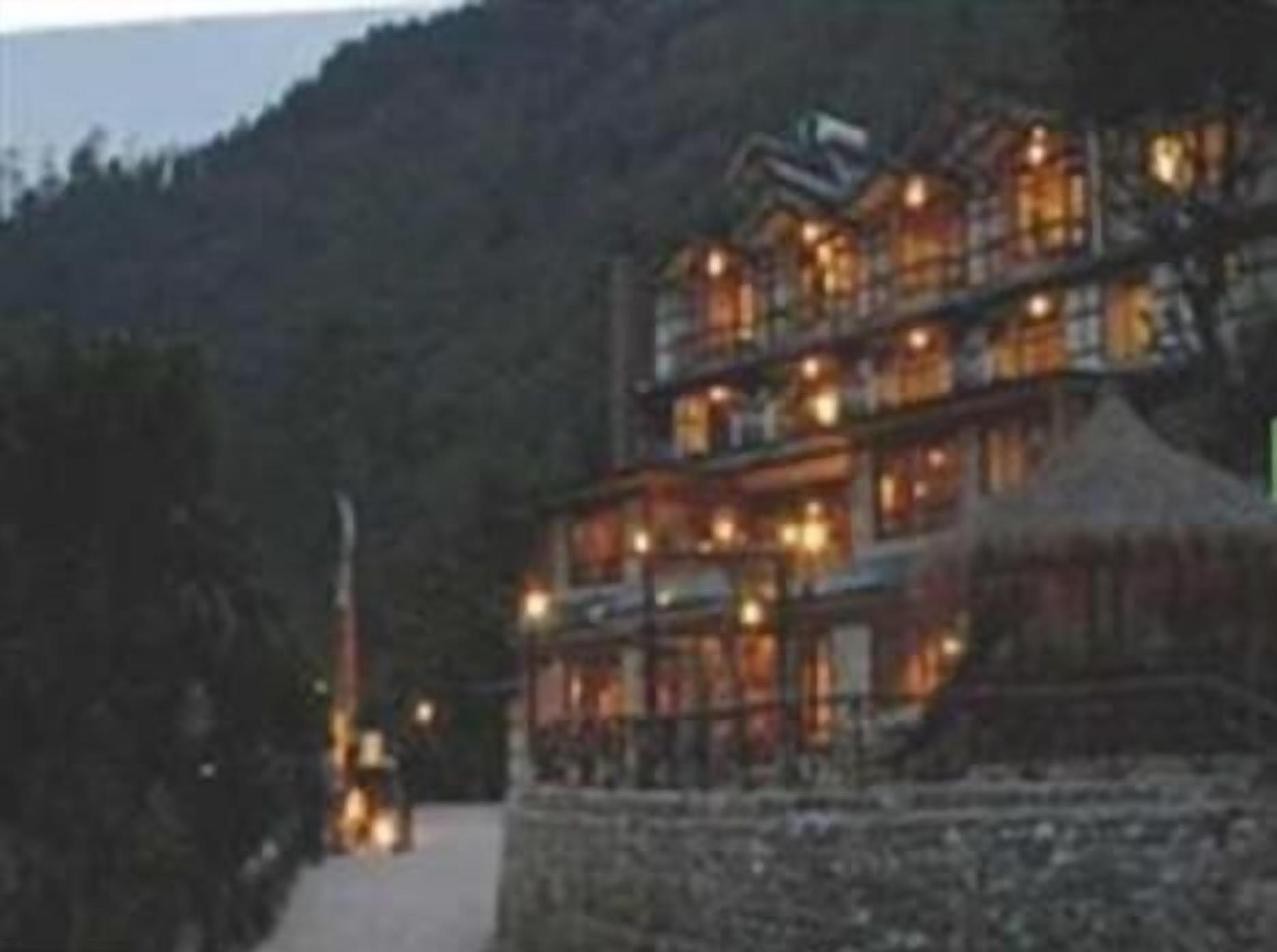A multi-story building with multiple windows and balconies, surrounded by a stone wall and a forested hillside.