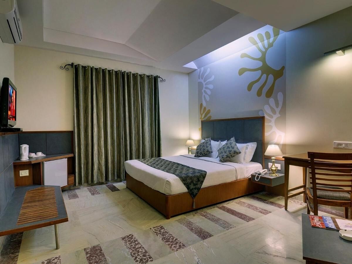 A hotel room with a bed, bedside tables, a desk, a chair, and a wall with a sun design.