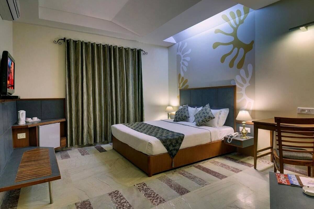Ein Hotelzimmer mit einem Bett, Nachttischen, einem Schreibtisch, einem Stuhl und einer Wand mit Sonnenelementen.