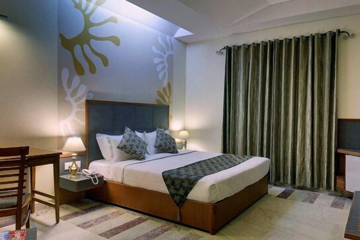 Ein Hotelzimmer mit Bett, Schreibtisch, Stuhl, Fernseher und Vorhang.