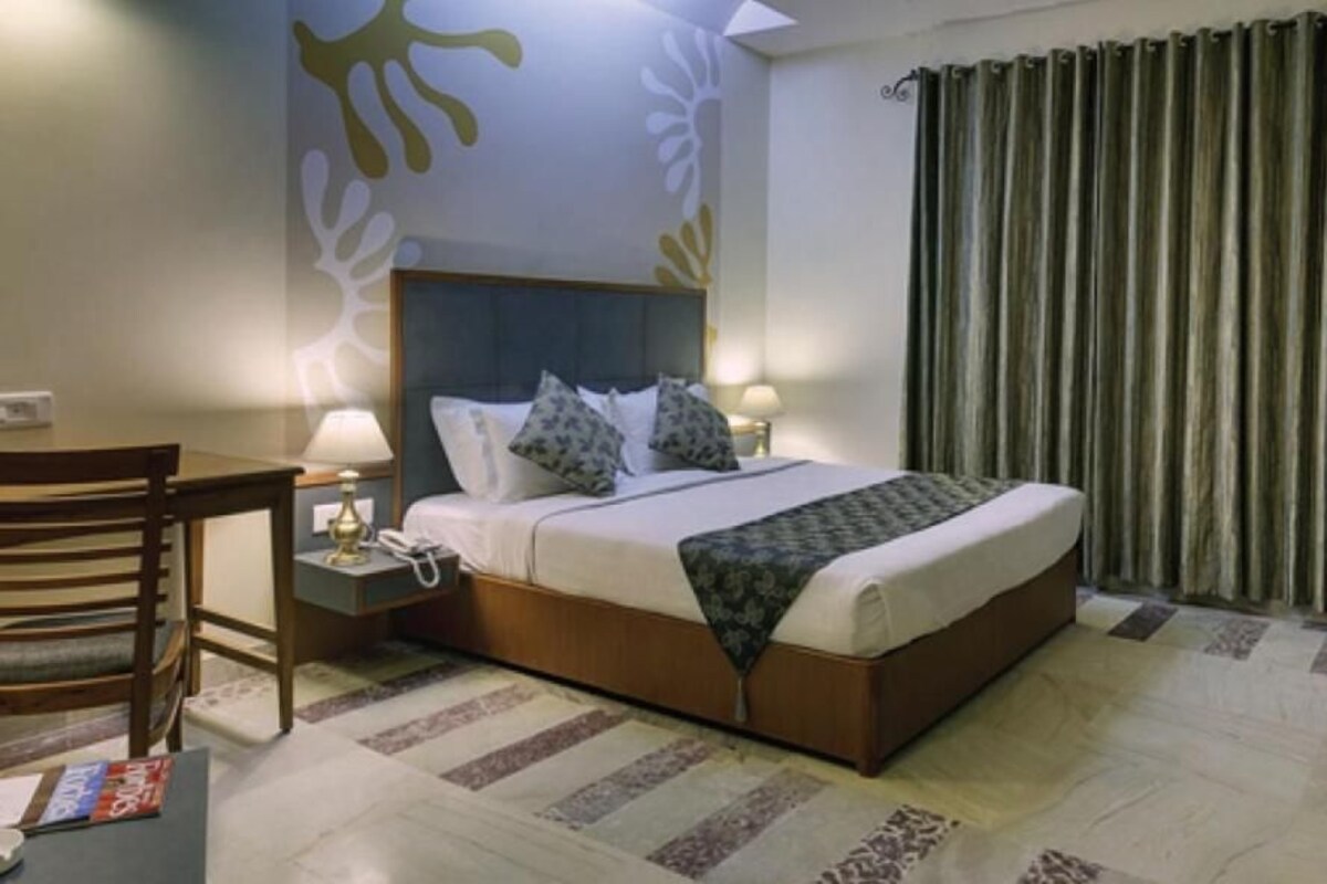 Una habitación de hotel con cama, mesita de noche, lámpara y televisor.