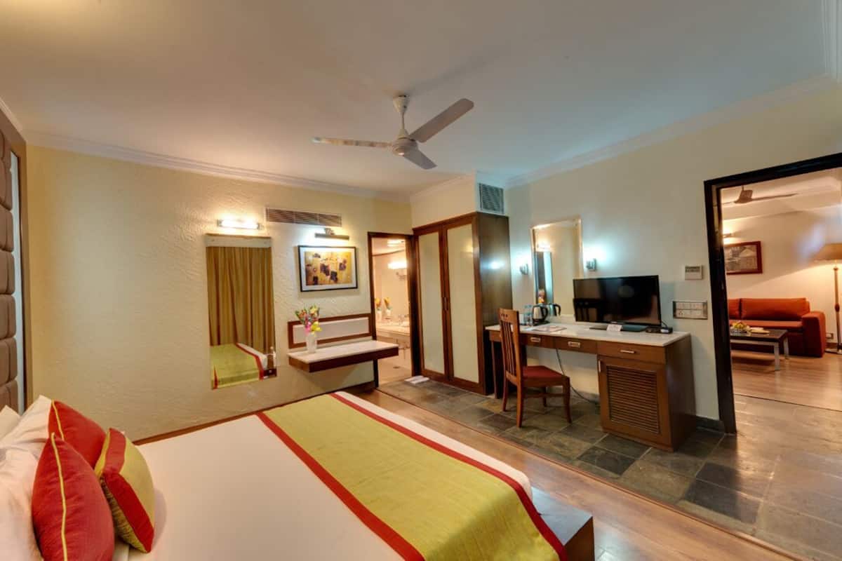 A hotel room with a bed, desk, TV, and seating area.