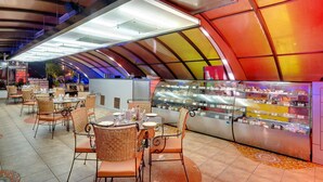 A restaurant with a curved ceiling, wicker chairs, and a glass display case filled with desserts. - Hotel Combermere (Shimla)