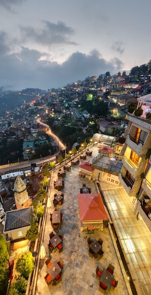 A rooftop terrace with outdoor seating, a view of a cityscape, and a prominent tower structure. - Hotel Combermere (Shimla)