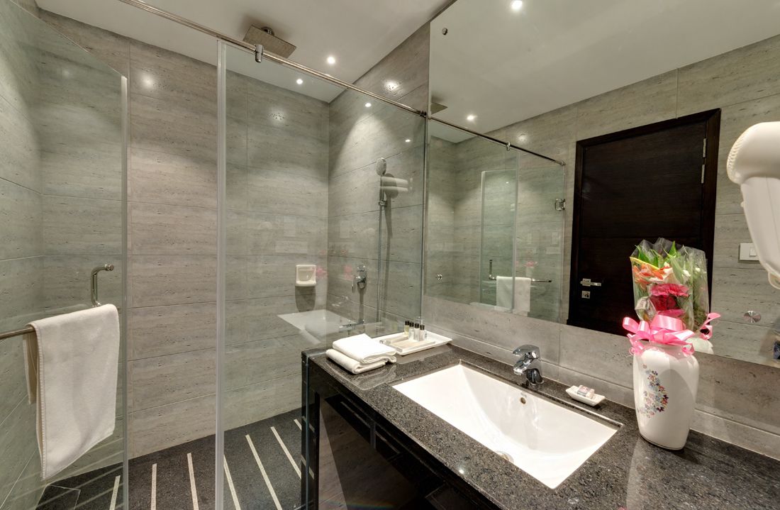 Un baño moderno con cabina de ducha de vidrio, un espejo grande, encimera de granito y un florero con flores.