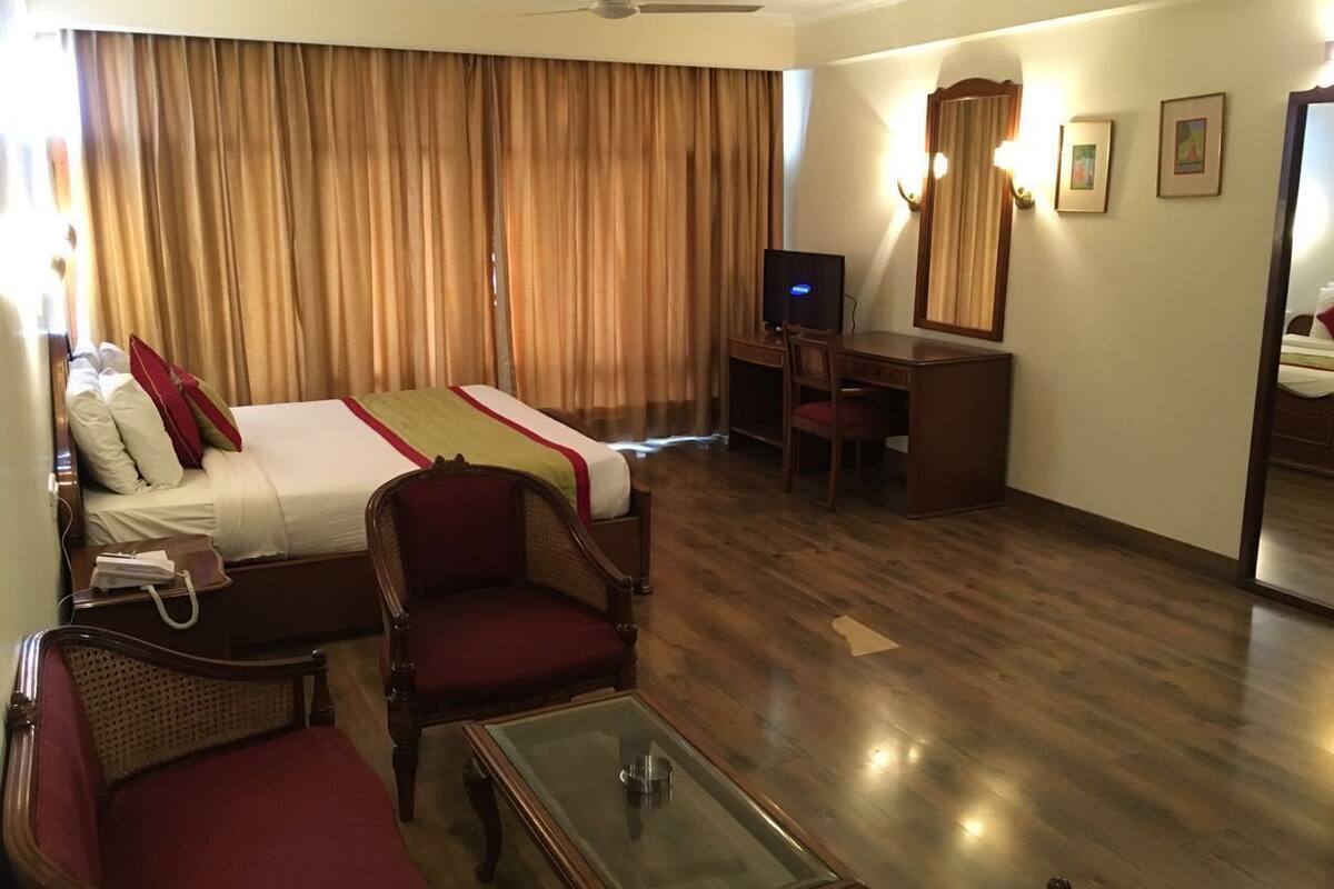 A hotel room with a bed, two armchairs, a desk, a television, and a mirror.
