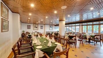 A dining area with wooden ceiling, tables set with white tablecloths and napkins, and chairs with green cushions.