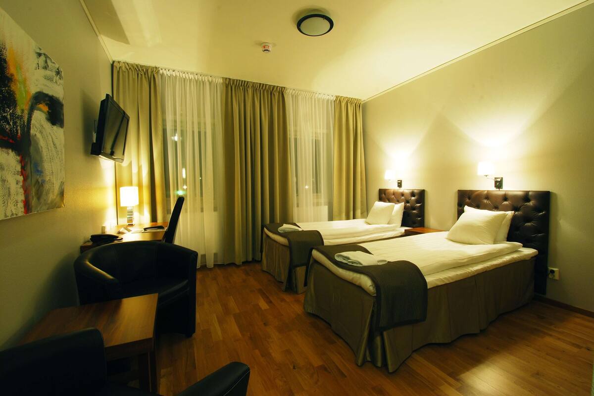 A hotel room with two beds, a desk, a chair, a TV, and a painting on the wall.