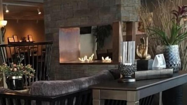 Un rincón acogedor con zona de estar y chimenea, una mesa con adornos, y una lámpara colgante.