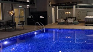 Una piscina interior con borde de azulejos, una recepción y un área de descanso con sillas y un sofá.