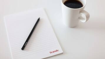 A white notepad with lined pages, a black pen, and a white cup of coffee on a white surface.