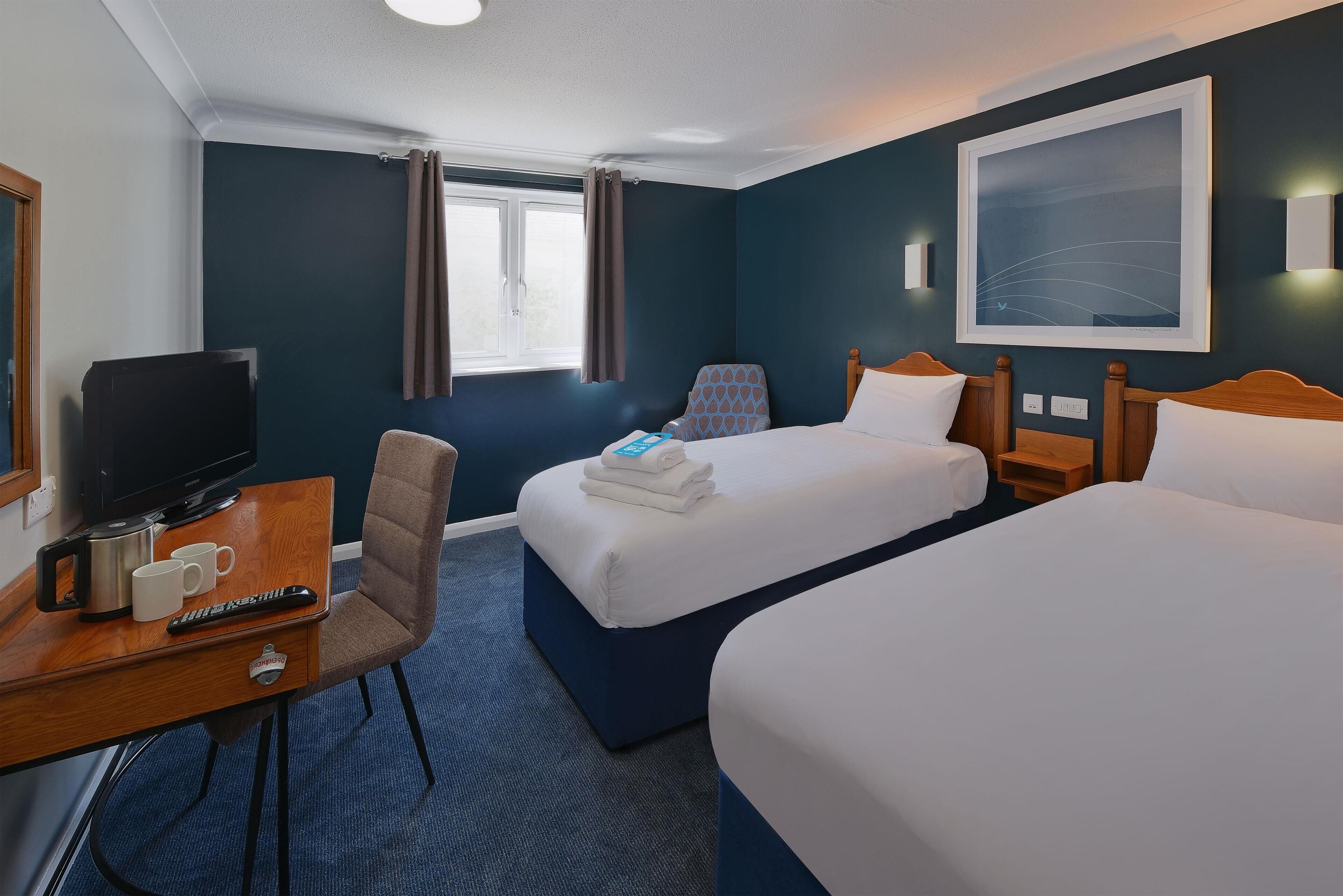 A hotel room with two beds, a desk with a television, remote controls, and a coffee maker.