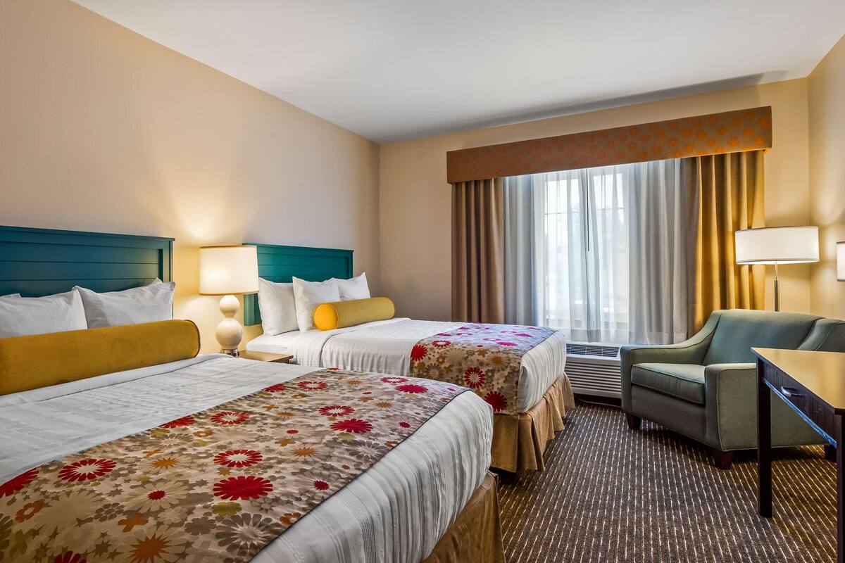 Une chambre d’hôtel avec deux lits, un canapé, un bureau et une grande fenêtre avec des rideaux.